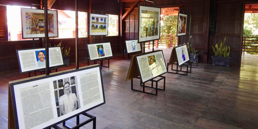 Slider Image A gallery with wooden floors and walls displaying several framed photographs with text.